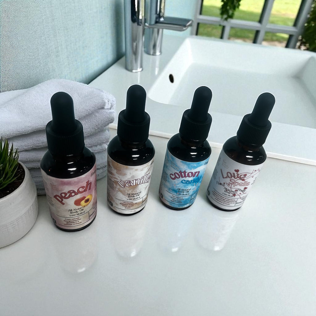 Collection of all natural body oils in dropper bottles labeled peach, vanilla, cotton candy, and lavender on bathroom counter