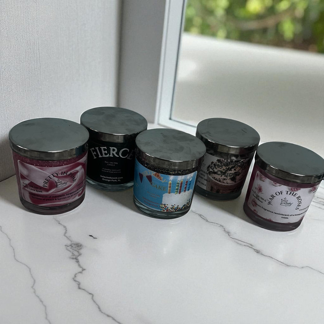 Collection of eco friendly specialty candles in glass jars with metal lids displayed on a marble countertop