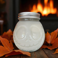 16 oz pumpkin spice candle cup with skull design and silver lid on wooden surface with autumn leaves
