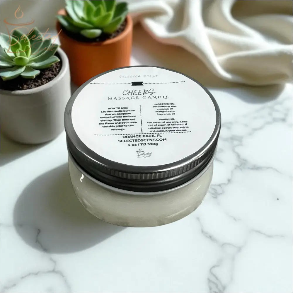 Selected Scent Cheers massage candle in a glass jar with metal lid with mango butter on marble surface