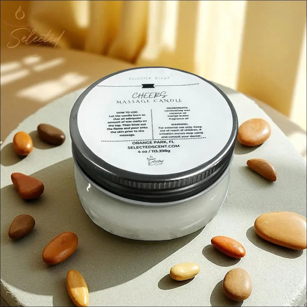 Selected Scent Cheers Massage Candle with Mango Butter in a clear jar with silver lid surrounded by smooth brown stones