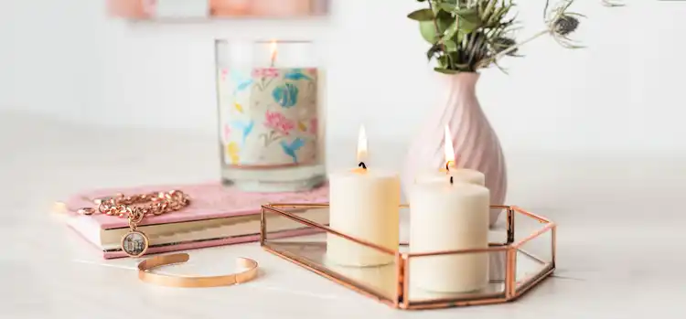 A collection of home decor items, including candles, jewelry, a notebook, and a vase with greenery.