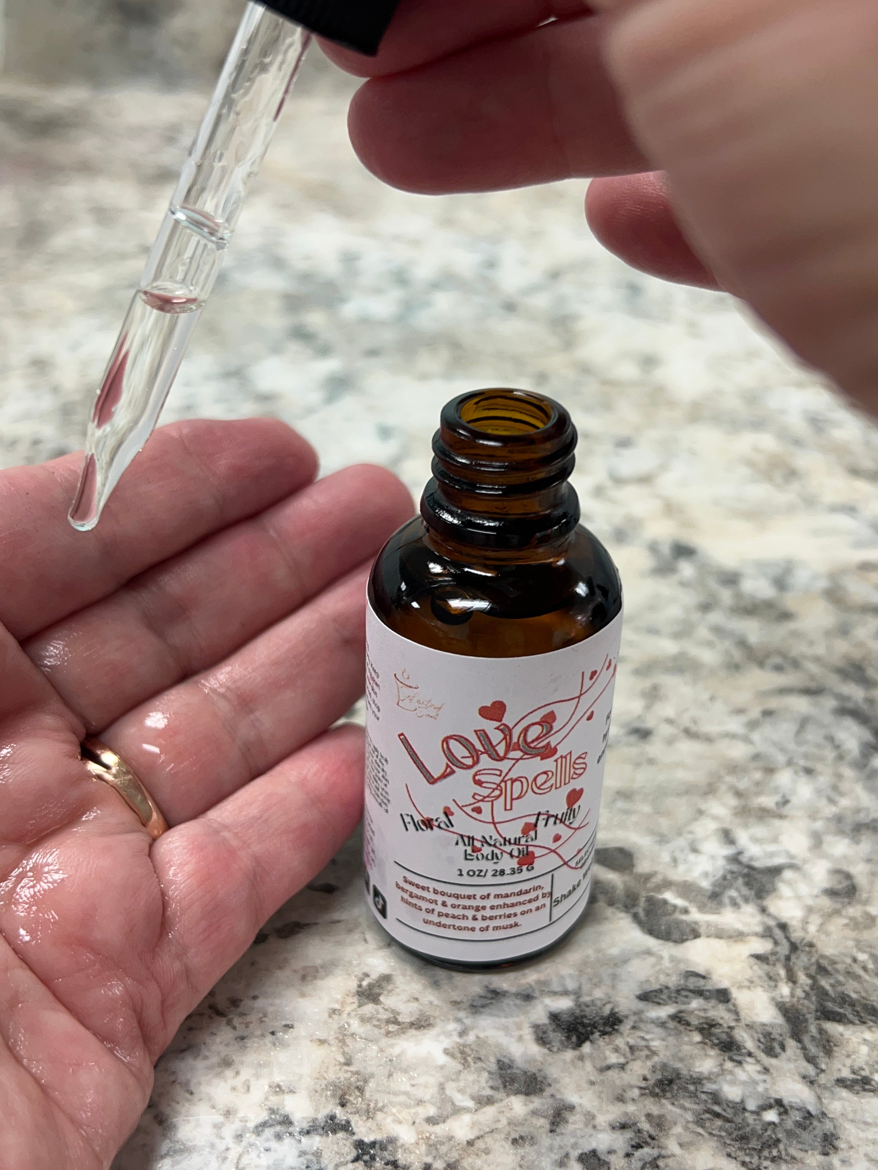Selected Scent Love Spells serum bottle with dropper dispensing hydrating and protecting oil onto hand