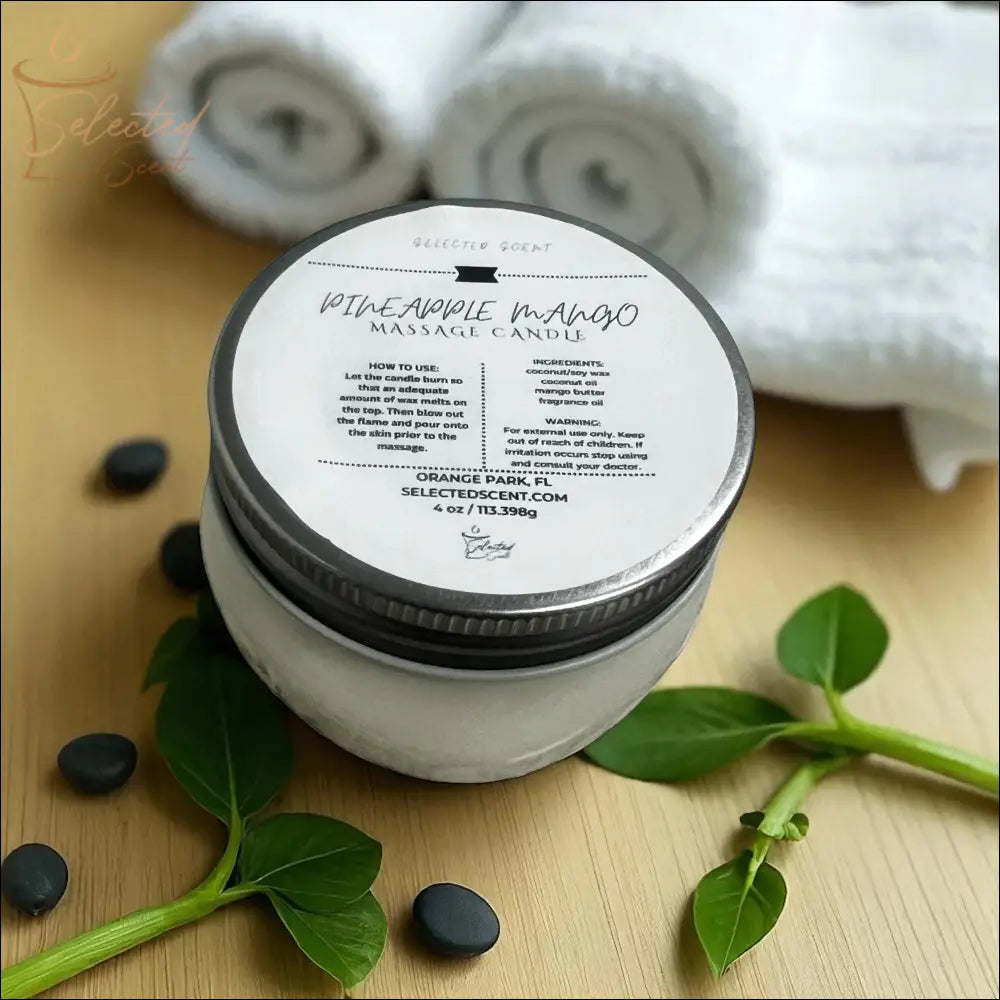 Selected Scent massage candle with mango butter in a glass jar on wooden surface with green leaves and black stones