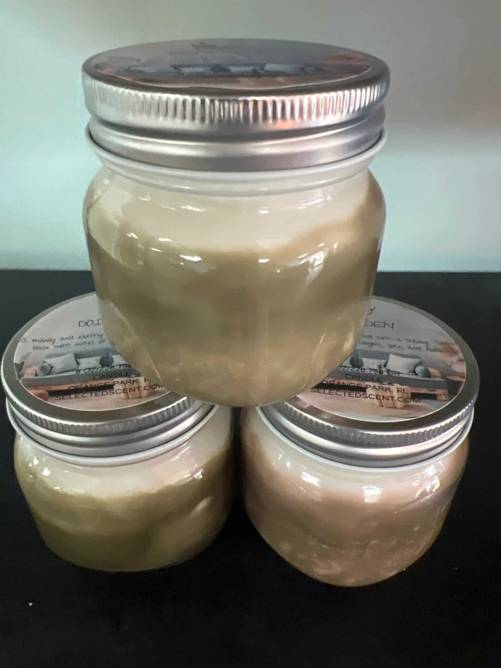 Selected Scent all natural masculine candle in glass jars with silver lids arranged in a pyramid on black surface
