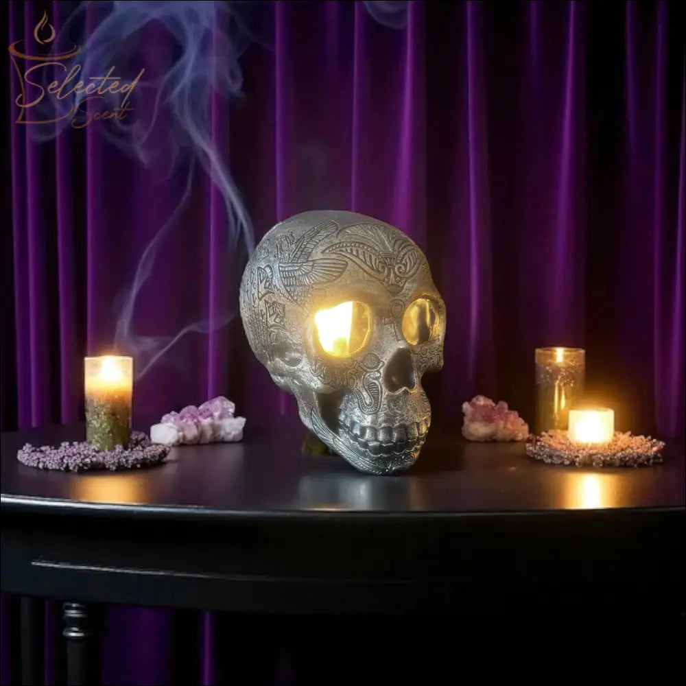 Selected Scent electric decorative warmer shaped like a detailed skull with glowing eyes on a black table with candles